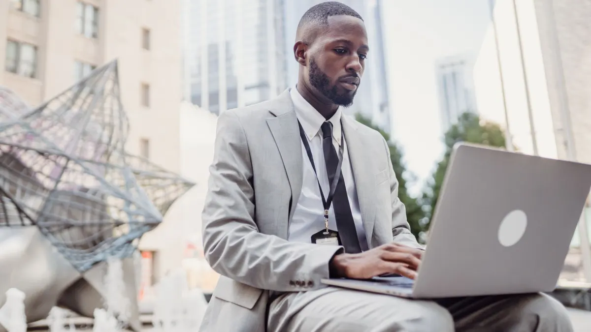 Business professional using a laptop in urban outdoor setting. Focused on remote work tasks.