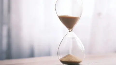 Minimalist hourglass filled with sand symbolizing time and patience, against a soft background.